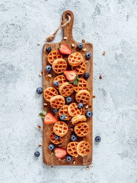 Small round delicious soft belgian waffles on cutting board. Fresh belgian waffles with berries and caramel sauce top view. Copy space for text or mock up. Vertical - Фото, зображення