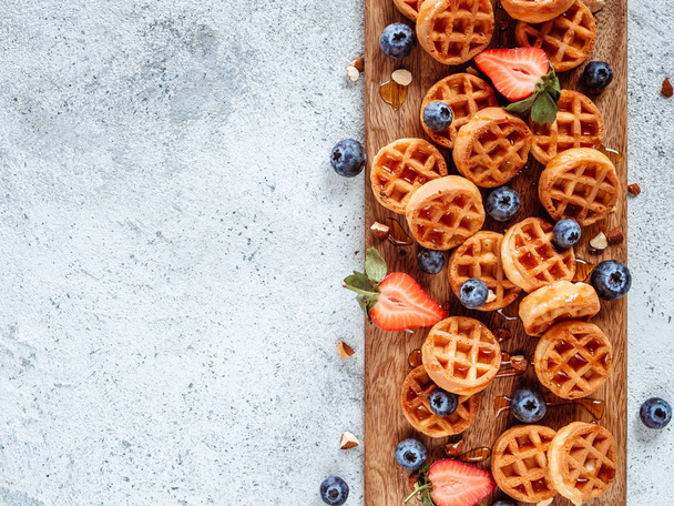 Small round delicious soft belgian waffles on cutting board. Fresh belgian waffles with berries and caramel sauce top view. Copy space for text or mock up - Фото, изображение