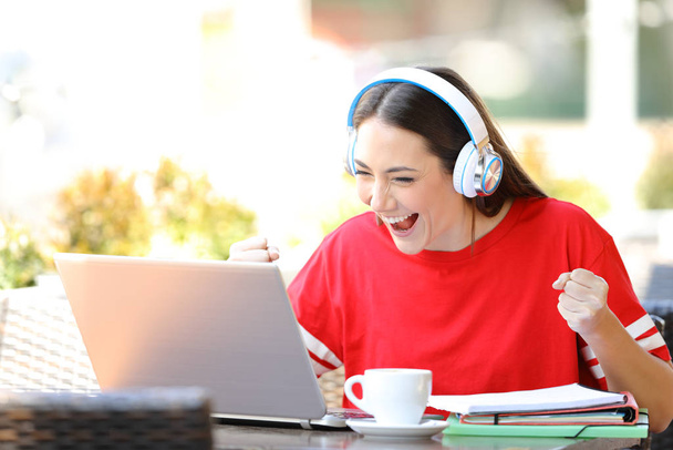 Excited student e-learning with a laptop and headphones finds offers in a coffee shop terrace - Photo, Image