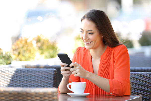 Happy woman is texting on smart phone sitting in a coffee shop terrace - Photo, Image