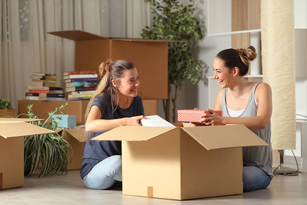 Two happy roommates talking unboxing gelongings moving home sitting on the floor - Foto, Bild