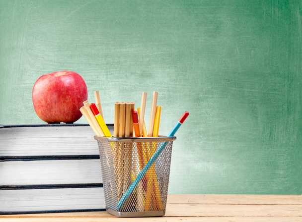 Pile of books with apple and pencils in basket container on wooden table with chalkboard background. Back to School concept - Photo, image