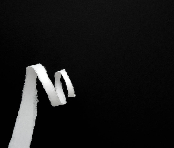torn off white paper strip and twisted on a black background, copy space - Fotografie, Obrázek