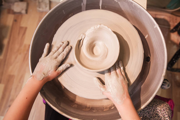 hands of young artist shaping clay on pottery wheel at workshop in ceramic studio  - Foto, Bild