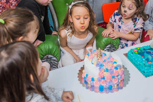 Little Girl Blowing Out Candle On Birthday Cake At Party In Playroom - Φωτογραφία, εικόνα