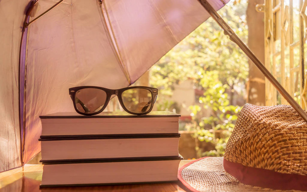 Defending light beams with umbrella. Umbrella protecting beautiful woman things. Books sunglasses and a straw hat. Summer holiday concept with copy space room for text. - Fotoğraf, Görsel