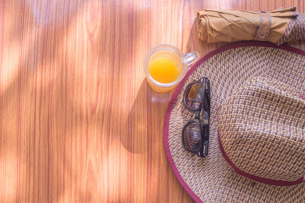 旅行の準備ができている。木製のテーブルに不可欠な現代の夏の女性の旅行アクセサリーのトップビューのビーチの背景。サングラス、傘、麦藁帽子とジュースのガラス。テキストのための部屋と休日のテーマ - 写真・画像