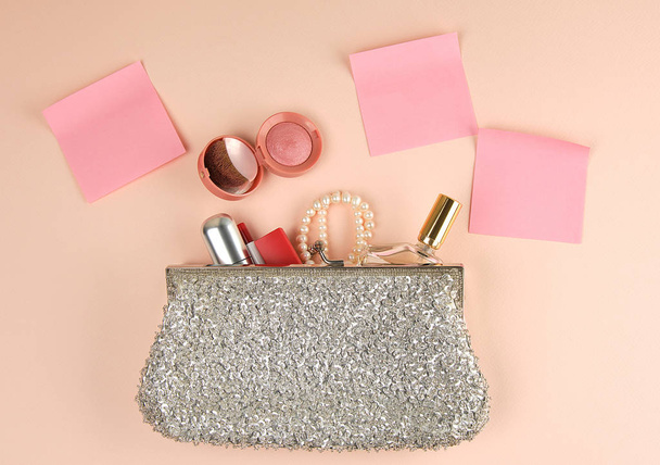 open silver clutch and cosmetics fell out of the middle, red lipstick,  peach background, top view - Fotó, kép