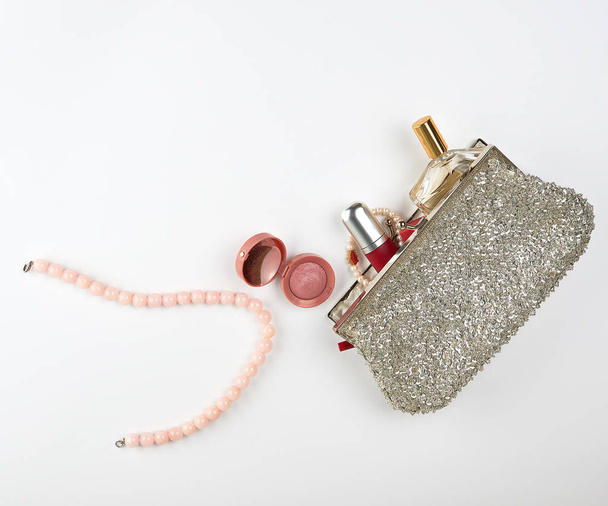 open silver cosmetic bag and women's cosmetics and perfumes, red lipstick, perfume and pearl pink beads on a white background - Foto, Bild