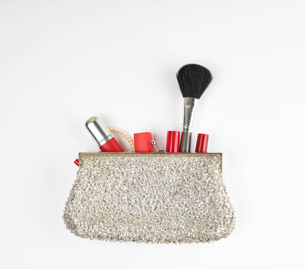 open silver clutch and cosmetics fell out of the middle, red lipstick, brush, white background, top view - Foto, Bild