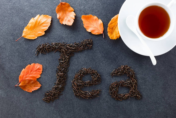 Folhas de chá preto soltas soletrar Chá na ardósia, folhas de outono e xícara de chá preto no lado, sobrecarga fotografada na ardósia (Foco Seletivo, Foco nas letras e nas folhas
) - Foto, Imagem