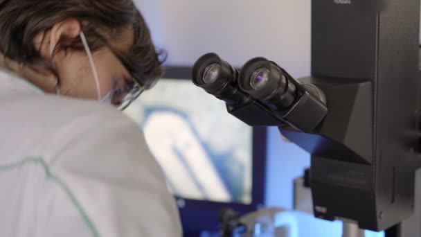 Scientist in a laboratory uses a microscope. Closeup shot - Felvétel, videó