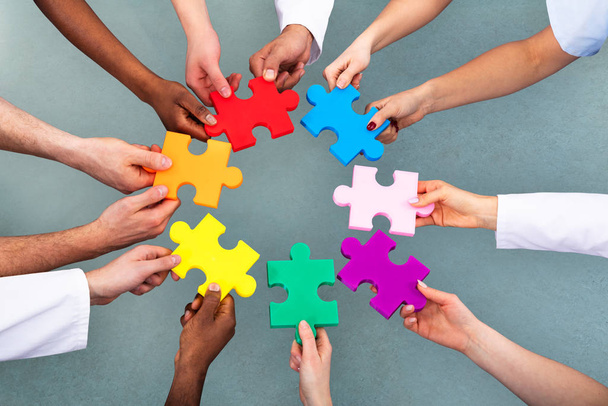 High Angle View Of Medical Team Solving Colorful Jigsaw Puzzle Against Grey Background - Fotoğraf, Görsel