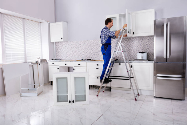 Widok tylny męskiego stolarza montującego białą szafkę na ścianie w kuchni - Zdjęcie, obraz