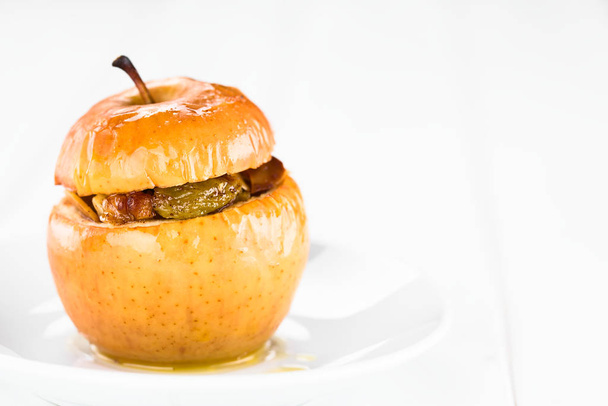 Fresh baked stuffed apple with walnut, almond, raisin, sultana, butter, sugar and cinnamon, a traditional autumn and winter dessert, photographed on white wood with copy space on the right side (Selective Focus, Focus on the front of the apple) - Φωτογραφία, εικόνα