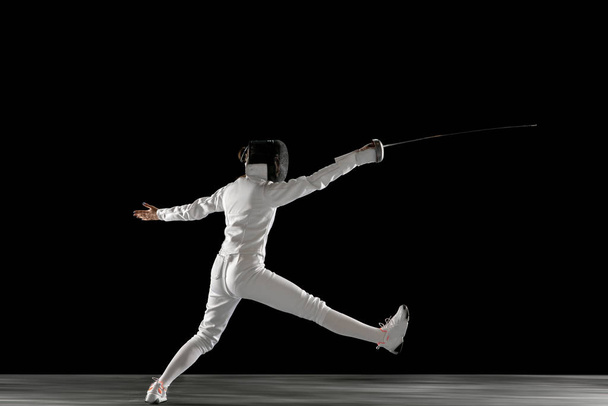 Teen girl in fencing costume with sword in hand isolated on black background - Foto, immagini