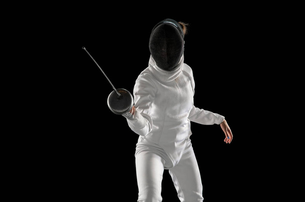 Teen girl in fencing costume with sword in hand isolated on black background - Фото, зображення