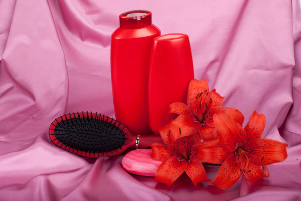 Care of hair. Shampoo, conditioner, hairbrush and lilies on the red satin. - Fotó, kép