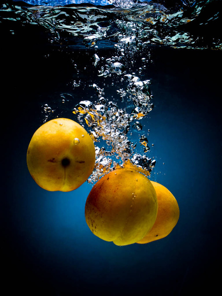 Fresh apricot in water on a black/blue background with air bubbles - Foto, Bild