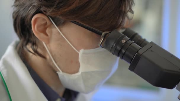 Scientist in a laboratory uses a microscope and takes notes. Closeup shot - Materiał filmowy, wideo