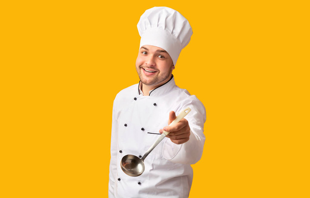 fröhlicher Koch mit Schöpflöffel vor gelbem Hintergrund posierend - Foto, Bild