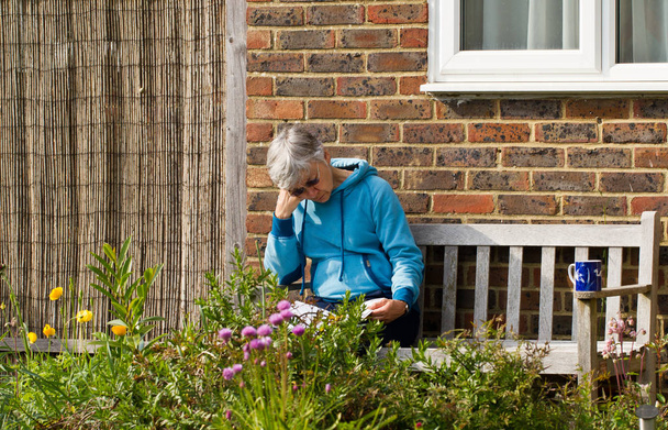 Senior woman sitting on bench reading in garden in summer sunshine - Foto, Bild