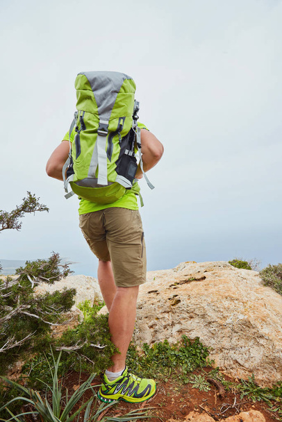 Un turista en una montaña con una mochila mira a la distancia
. - Foto, Imagen