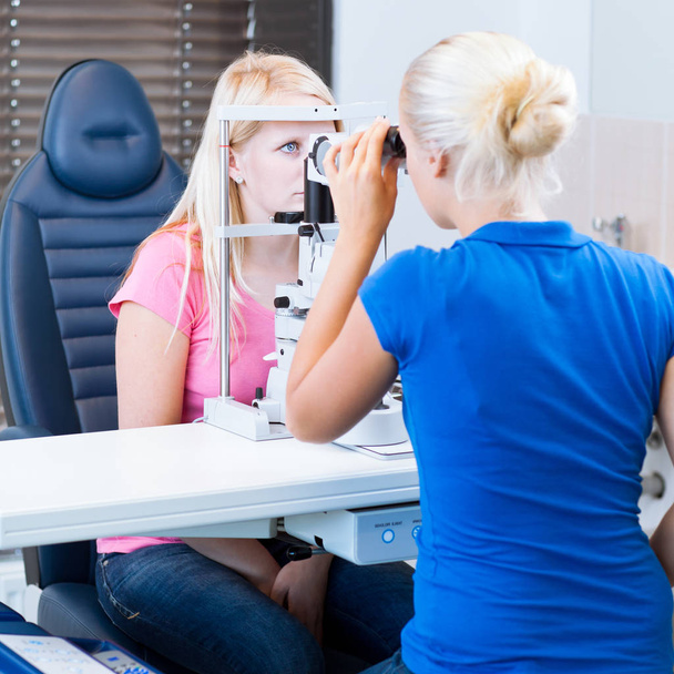 optometry concept - pretty young female patient having her eyes examined by an eye doctor/optometrist (color toned image - Foto, imagen