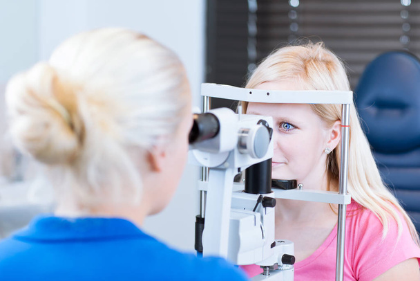 optometry concept - pretty young female patient having her eyes examined by an eye doctor/optometrist (color toned image - Фото, изображение