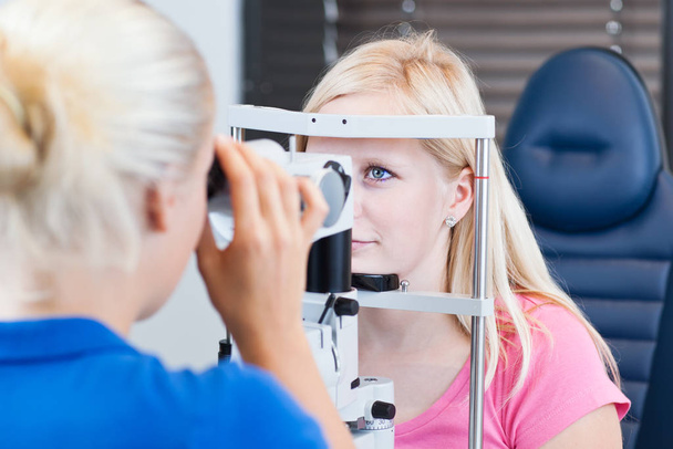 optometry concept - pretty young female patient having her eyes examined by an eye doctor/optometrist (color toned image - Фото, зображення