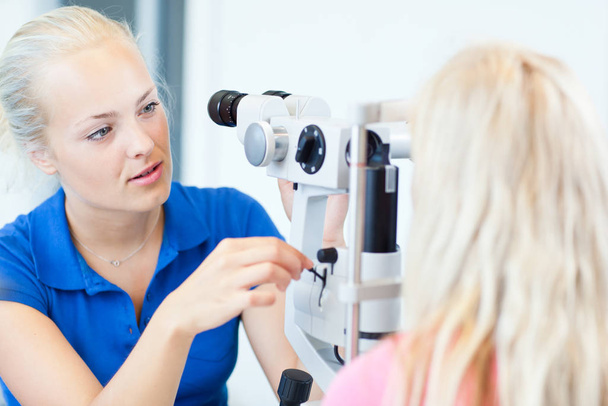 optometry concept - portrait of a pretty young optometrist using a slit lamp to check her patient&#039 - Photo, Image