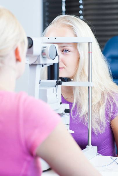 optometry concept - pretty young female patient having her eyes examined by an eye doctor/optometrist (color toned image - Фото, зображення