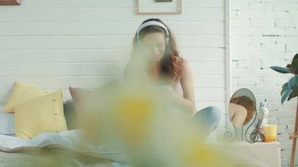 Mosolygó terhes nő zenét hallgat az ágyban. A várandós anya bent pihen. - Felvétel, videó