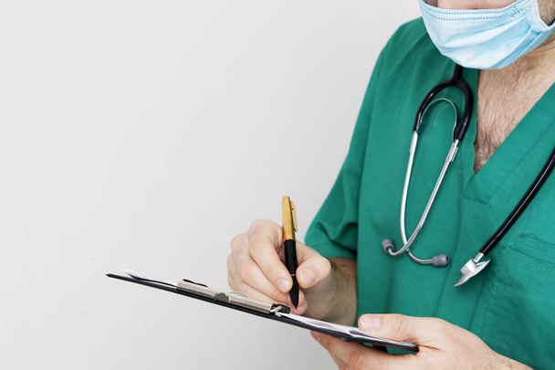 ein Arzt in Uniform, eine Maske mit Stethoskop, schreibt auf einen Zettel - Foto, Bild