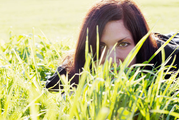young woman lying in a summery green meadow. closeup with focus on the eye. - Foto, imagen