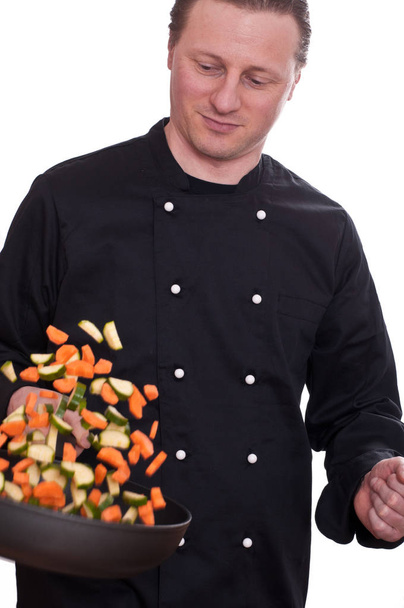 a cook turns by raising the vegetables in a frying pan - Fotó, kép