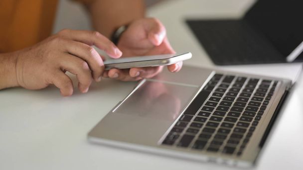 Вид сбоку мужчины-фрилансера, сидящего на смартфоне во время работы на ноутбуке и планшете в простом рабочем пространстве
 - Фото, изображение