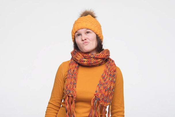 Портрет задумчивой молодой женщины в теплом шарфе и шляпе, смотрящей вверх
 - Фото, изображение