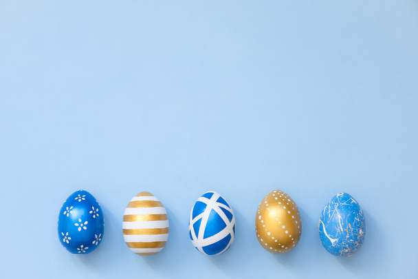 Wielkanoc ozdobione jaja na niebieskim tle. Minimalna koncepcja Wielkanocy. Szczęśliwej kartki wielkanocnej z miejsca na tekst. Widok z góry, płaski.  - Zdjęcie, obraz