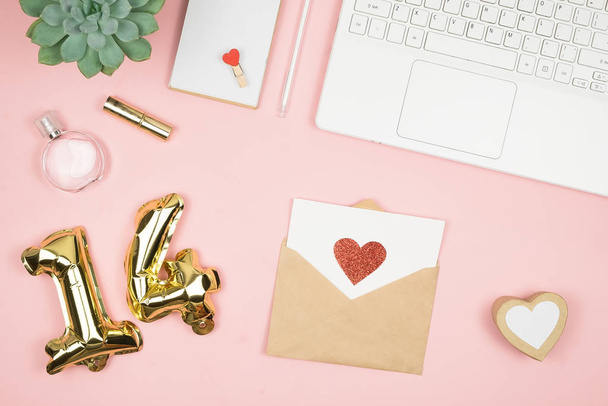 Flat lay home office desk. Women workspace with laptop, cosmetics, perfume, accessories on pink background. Love letter envelope, valentine red heart - Fotó, kép