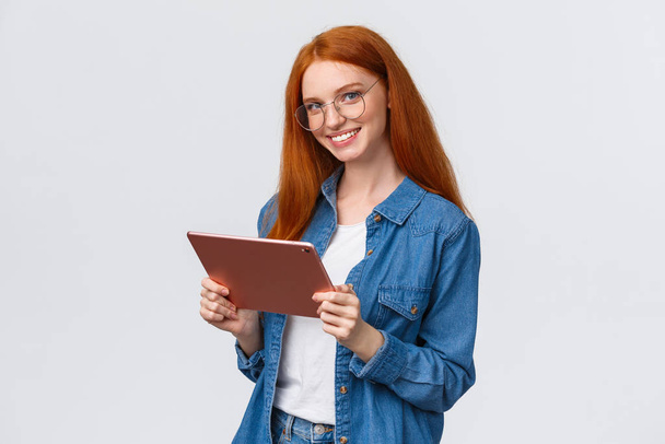 Professionalità, lavoro e concetto di persone. Giovane allegra rossa attraente femminile in occhiali, tenendo tablet digitale e sorridendo alla fotocamera con felice espressione fiduciosa su sfondo bianco - Foto, immagini