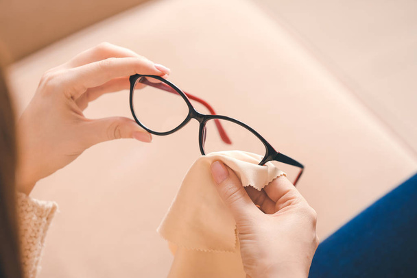 Young woman wiping eyeglasses at home, closeup - Foto, afbeelding