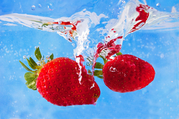 Fresh strawberries falling into the water on a blue mosaic background - 写真・画像