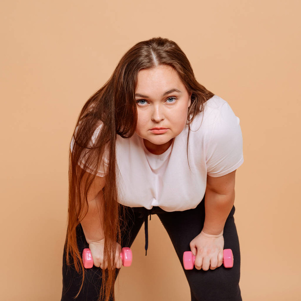 Bent over girl with dumbbells on beige background - Photo, image