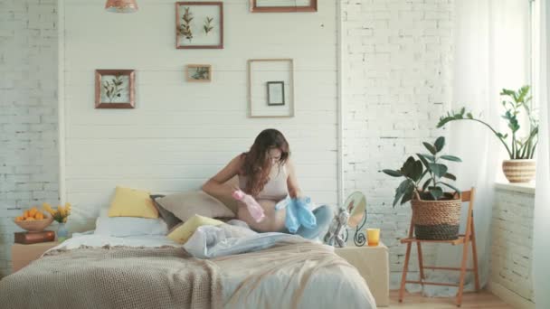 Joyful belly mother looking baby clothes. Happy pregnant sitting bedroom. - Video, Çekim