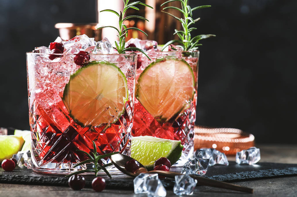 Glasses of cranberry drink or cocktail with rosemary, cranberries, vodka and crushed ice on grey background, copper bar tools, copy space - Φωτογραφία, εικόνα