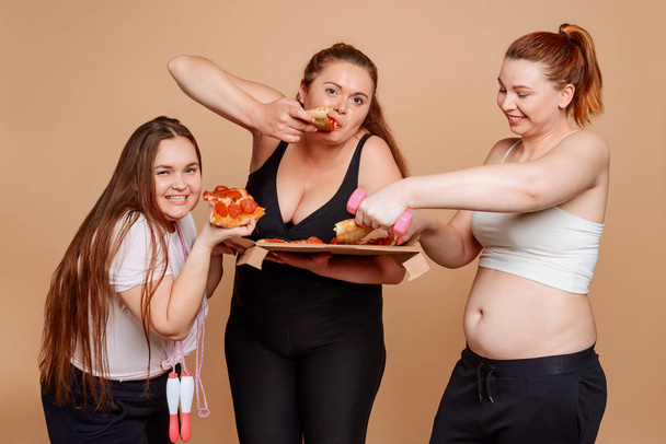 Three overweight women eating pizza right after workout - Foto, Imagen