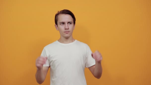 man in wit t-short op gele achtergrond heft zijn hand omhoog - Video