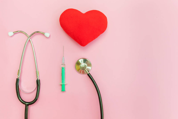 Equipo de medicina estetoscopio o jeringa fonendoscopio y corazón rojo aislado sobre fondo rosa pastel de moda
 - Foto, imagen