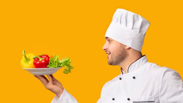 Кухар Хлопець тримає тарілку з овочами на жовтому тлі, вид збоку
 - Фото, зображення